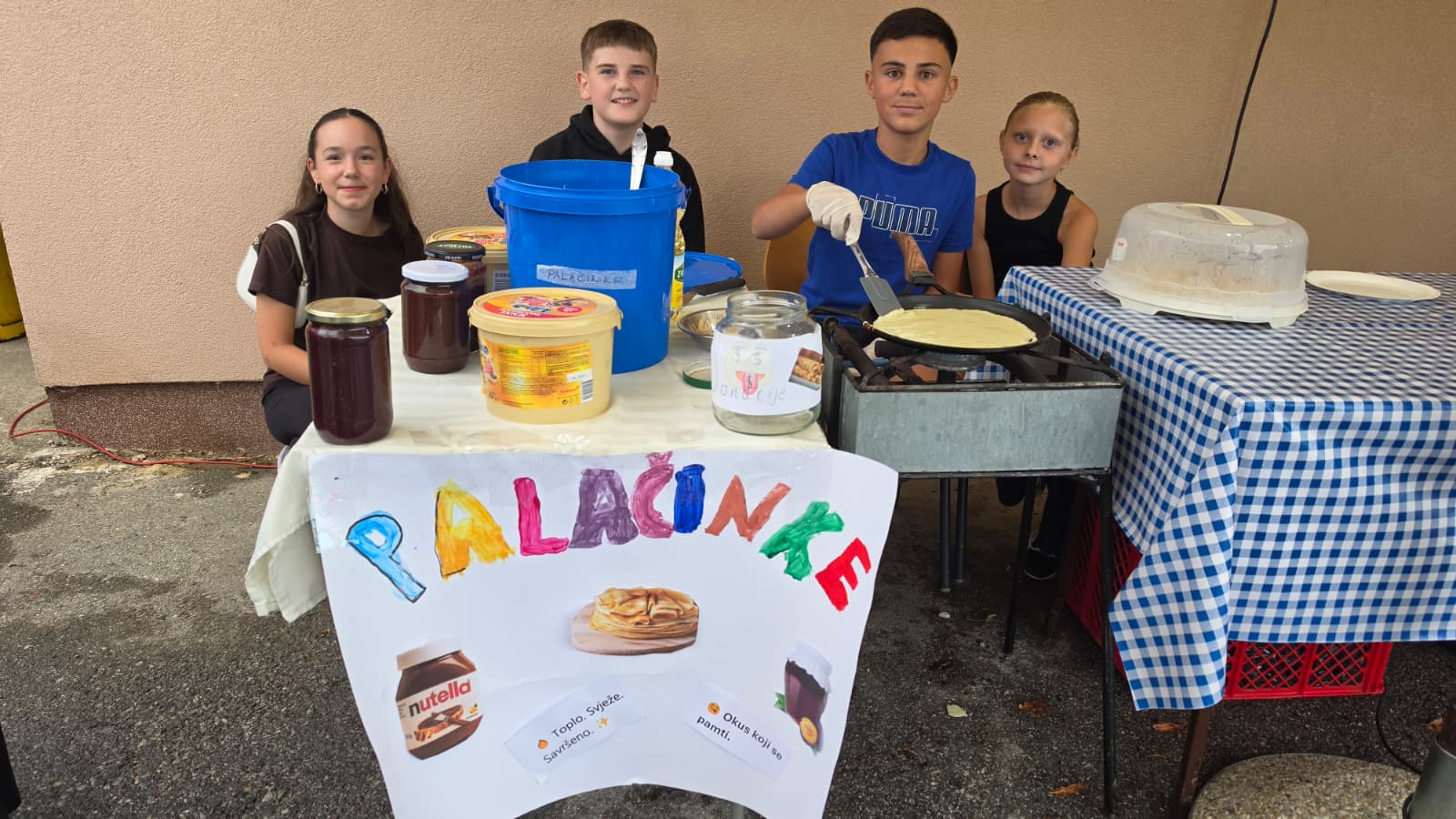 Djeca za štandom palačinki uz šareni plakat