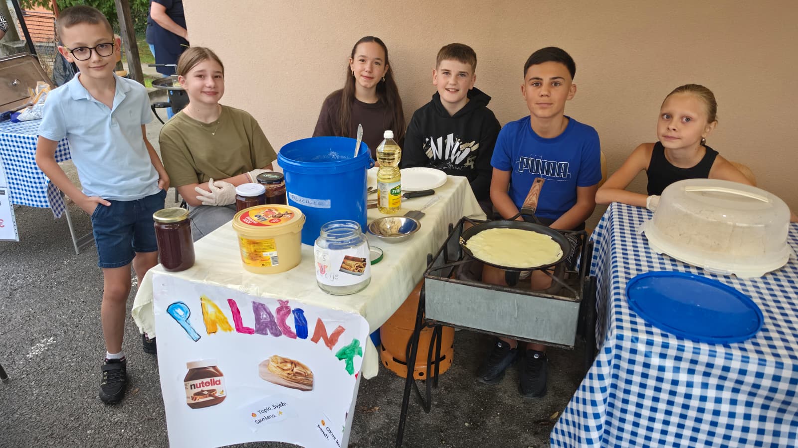 Djeca i mladež DVD-a Dropkovec za svojim štandom s palačinkama uz šareni plakat Palačinke