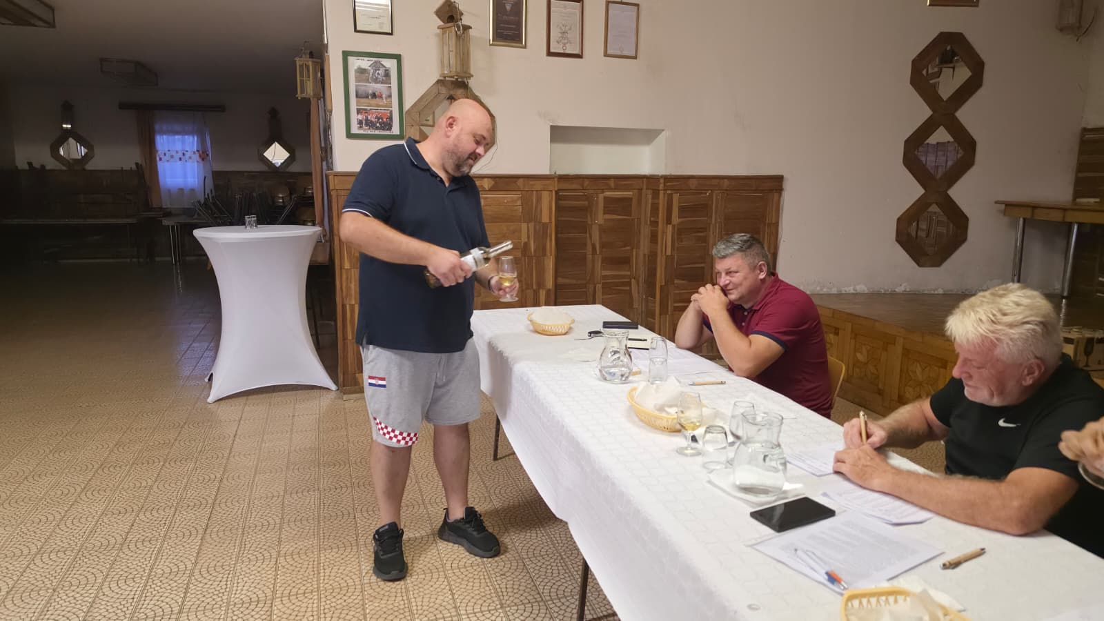 Član DVD-a Dropkovec toči uzorak rakije u čašu ocjenjivača za stolom stručnog povjerenstva